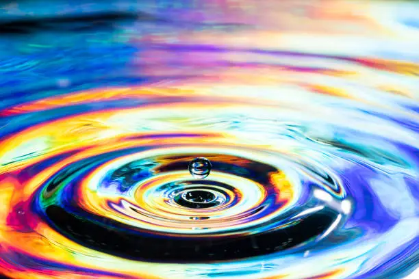 Color pool Drop of water landing in multi-colored pool of water creating ripples.